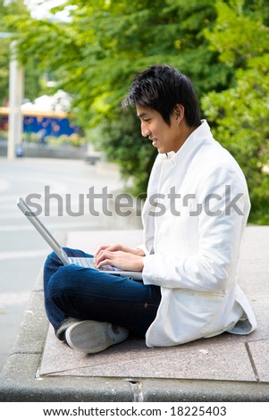 An asian college student working on his laptop at the campus