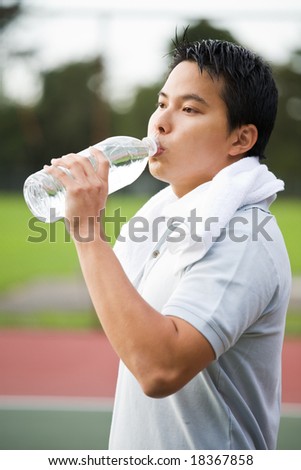 A young sporty active Asian male drinking water after exercise