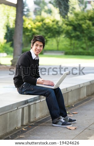 An asian student working on his laptop on campus
