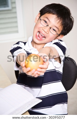 A shot of an asian kid studying and holding an apple at home