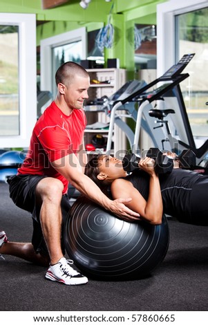A shot of a male personal trainer assisting a woman lifting weights