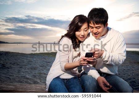 A shot of an asian couple on the phone reading text messages