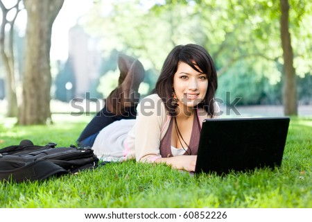 Mixed race college student lying down on the grass working on laptop at campus