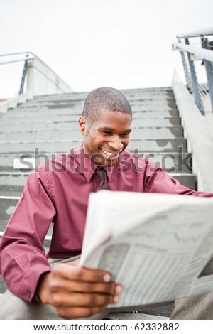 A portrait of a smiling black businessman reading newspaper outdoor