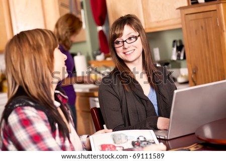 A shot of two sisters talking in the kitchen while their mom cooking in the background
