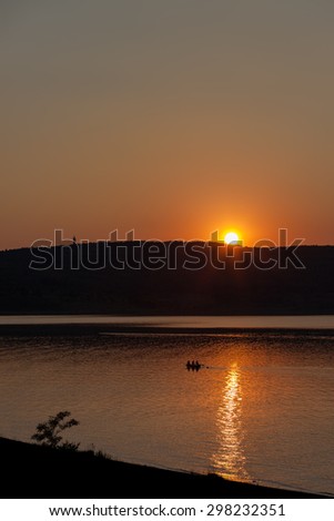 Beautiful, warm sunset over a large lake. Tiny boat with people on board flowing at sunset by the lake.