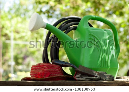 garden watering can, shovel, hat, gloves and a garden hose in the garden