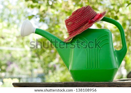 Garden watering can in the garden green and red hat