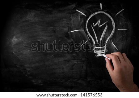 man draws a chalk lightbulb on a black school board