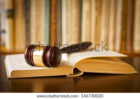 Open law book with a judges gavel resting on top of the pages in a courtroom or law enforcement office