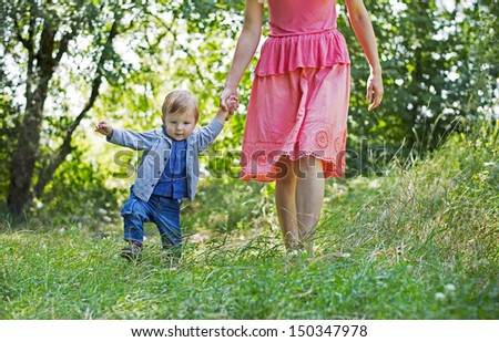 young mom teaches young boy walking and leads him by the hand outdoors