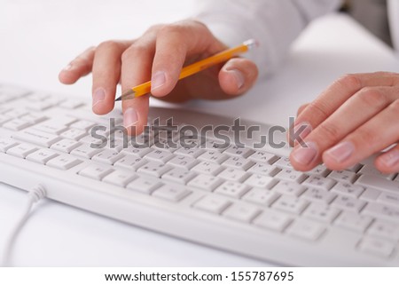 Man typing on a computer keyboard at work holding a pencil in the fingers of one hand as he enters data, close up view