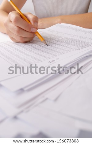 Hands holding a large, unsorted batch of loose paperwork in the office with printed tables of statistics