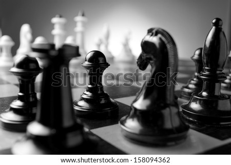 Close up low angle corner view of chess pieces lined up on a chess board ready for a game with focus to a black pawn with a castle and knight in the foreground