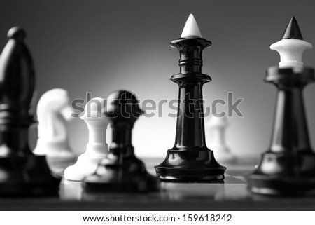 Low angle black and white image of a game of chess with focus to a single chess piece conceptual of planning, strategy and skill needed to beat the competition and win