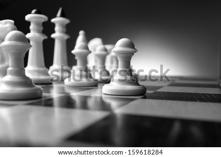 Planning a strategy in chess with a low angle view in black and white of chess pieces on a chessboard with selective focus to a pawn