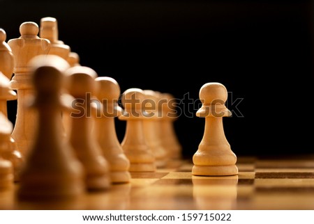 Playing a game of chess with a low angle view of vintage wooden chess pieces on a reflective surface with focus to a single pawn in the foreground and shallow dof