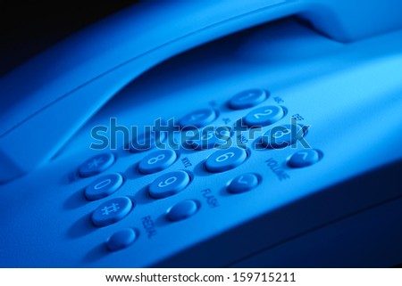 Close up view of the handset and keypad of a dial up telephone instrument with focus to the keys on the keypad in blue light