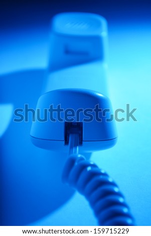 Telephone handset and cord lying upside down on a flat white surface in blue light, close up view down the length of the receiver with shallow dof