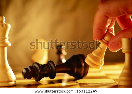 Man making a move in a game of chess knocking over a chess piece with a pawn that he is holding in his hand, close up view of the chess board