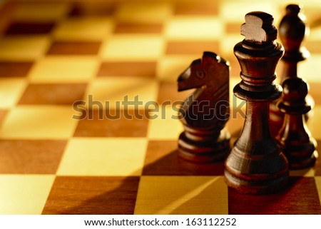 Dark wood chess pieces standing on a chessboard in a low angle beam of light with focus to the king and a large area for copy