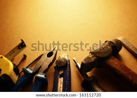 Sepia toned image of a toolkit for home maintenance with a screwdriver, hammer, pliers, knife, tape measure and nails arranged in a semi circle with copyspace