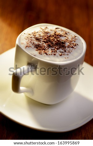 Sweet coffee with cream and chocolate flakes, in an elegant white cup with saucer, on wooden table