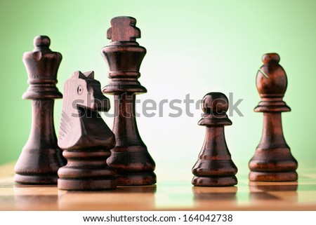Wooden dark chess pieces on a chessboard against a green background with a king, queen, bishop, knight and pawn