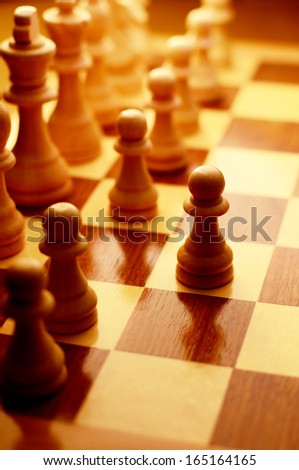 Playing a game of chess with chess pieces lined up on a chessboard with focus to a single pawn that has been advanced to the next row, high angle view