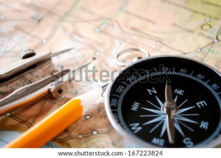 Conceptual image of a magnetic compass and pencil lying on a map for plotting a journey, geocaching or orienteering where it is used as a navigational instrument