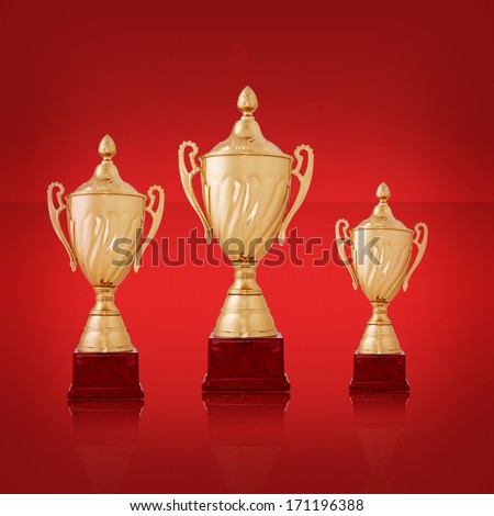 Three golden trophies on a bright red background of varying sizes waiting to be awarded to the three winners in a competition, with copyspace