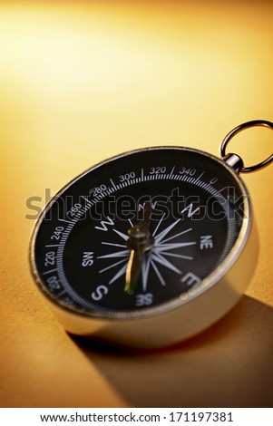 Handheld magnetic compass for navigating via the earths magnetic field lying on a graduated gold background with copyspace