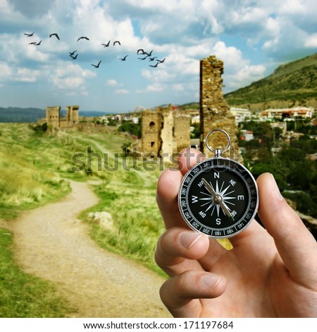 Conceptual image of the hand of a man using a compass to navigate and find the direction while sightseeing abroad with the ruins of an ancient castle in the background