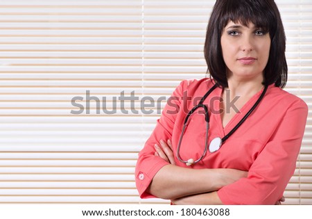 Beautiful confident young female doctor standing with a stethoscope around her neck looking intently at the camera with folded arms