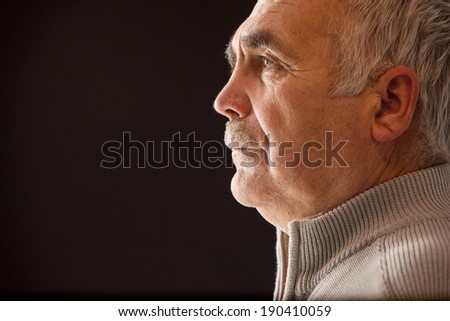 Beautiful portrait of a pensive senior man with a moustache in profile on a black background with copyspace staring straight ahead as he reminisces on his life