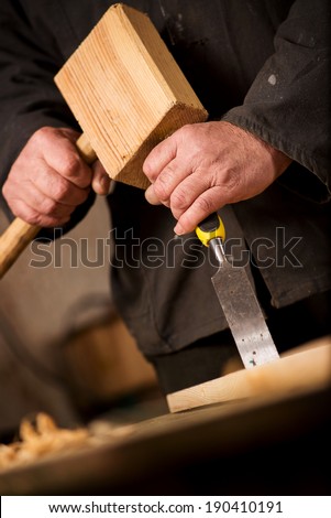 Close up of the hands of a carpenter or joiner using a chisel and wooden mallet to cut and shape a piece of wood in a woodworking workshop