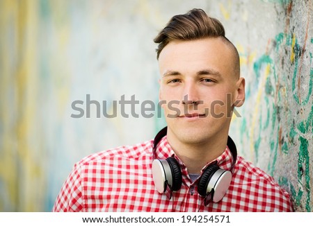 Handsome young man wearing headphones slung around his neck looking at the camera with a pensive speculative expression
