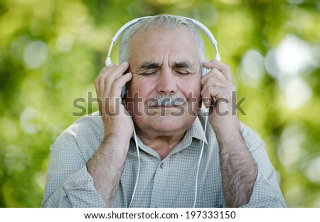 Pensioner enjoying his music sitting with his eyes closed in pleasure as he listens to a tune on his headphones while sitting out in the garden