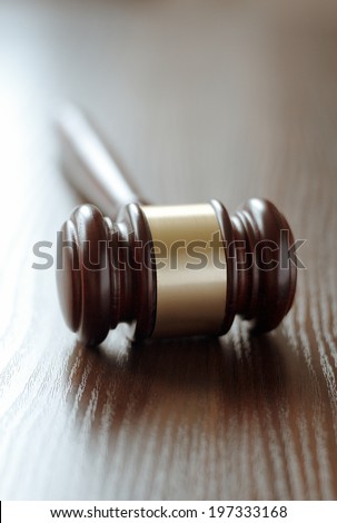 Wooden judges gavel with a central brass band around it lying with the handle facing away on a wooden desk or table with shallow dof conceptual of law enforcement and judgements in court