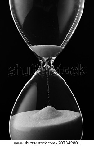 Sand running through the bulbs of an hourglass measuring the passing time in a countdown to a deadline, on a dark background with copyspace