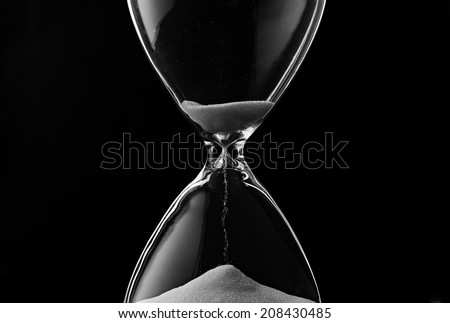 Sand trickling through the bulbs of an hourglass or egg timer measuring the passage of time on a dark background