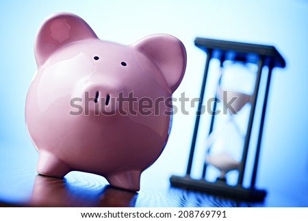 Close-up of a pink porcelain piggy bank with a vintage hourglass behind, concept of saving money and passing time