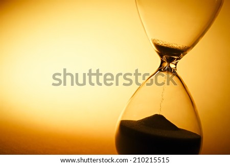 Sand passing through the glass bulbs of an hourglass measuring the passing time as it counts down to a deadline or closure on a yellow background with copyspace