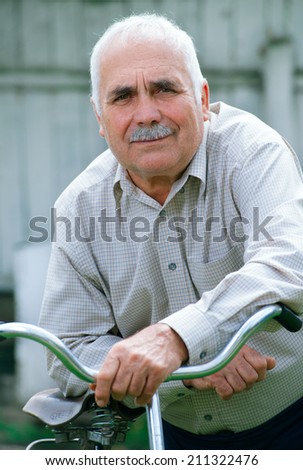 Portrait of an active senior retired man leaning on the handlebar of his bicycle, outdoors