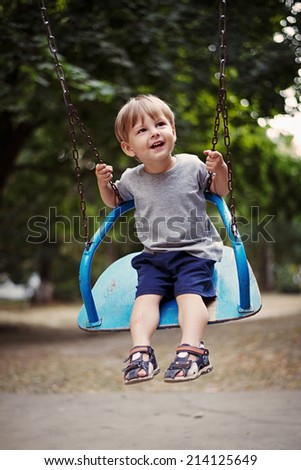 Happy little boy swinging on a swing outdoors in the garden or park smiling with enjoyment as he looks up watching something off frame