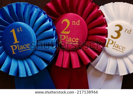 Three winners rosettes for first, second and third place in pleated blue, red and white ribbon respectively with central text
