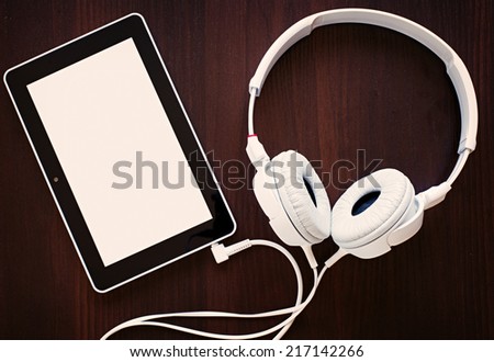 Set of modern white headphones attached by a cable to an MP3 player with a blank white screen visible to the viewer in a music and audio concept, on black