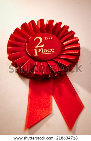 2nd place winners rosette in red with gold text made of pleated ribbon to be awarded to the runner up in a competition, close up view