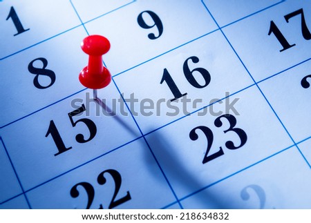 Red pin marking the 15th on a calendar as a reminder of an important event, close up low angle view