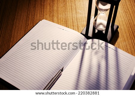 Hourglass Casting Shadow on Lined Notebook with Pen on Desk as seen from Above in Time Concept Image